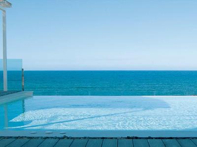 Infinity-Pool mit Meerblick und Sitzbereich im Freien unter klarem Himmel.