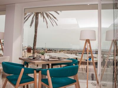 Zona pranzo moderna con sedie blu e vista mare dietro parete di vetro.