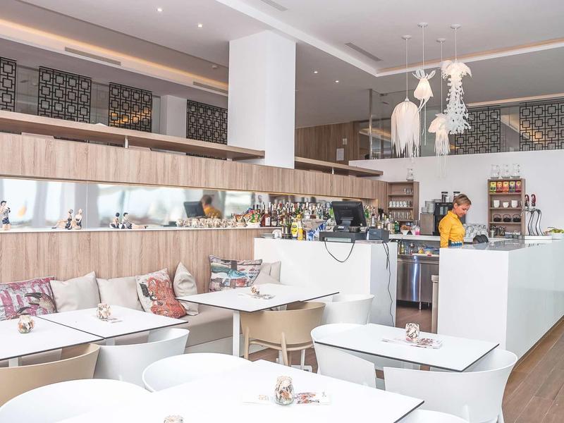 Caffè moderno con interni in legno chiaro e tavoli bianchi in un'atmosfera rilassata.