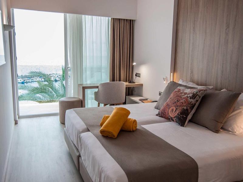 Camera d'hotel moderna con letto matrimoniale, scrivania e balcone con vista sul mare.