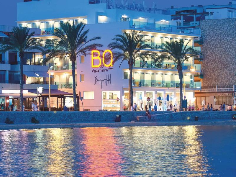 Edificio dell'hotel illuminato vicino all'acqua con palme e luce riflessa sul mare al crepuscolo.
