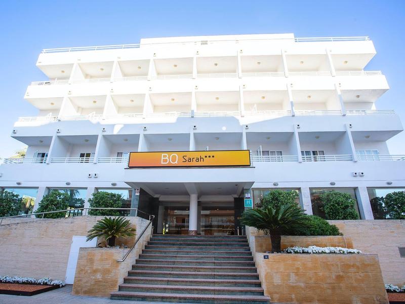 Weißes mehrstöckiges Gebäude mit Balkon, Treppe und orangem Schild am Eingangsbereich.