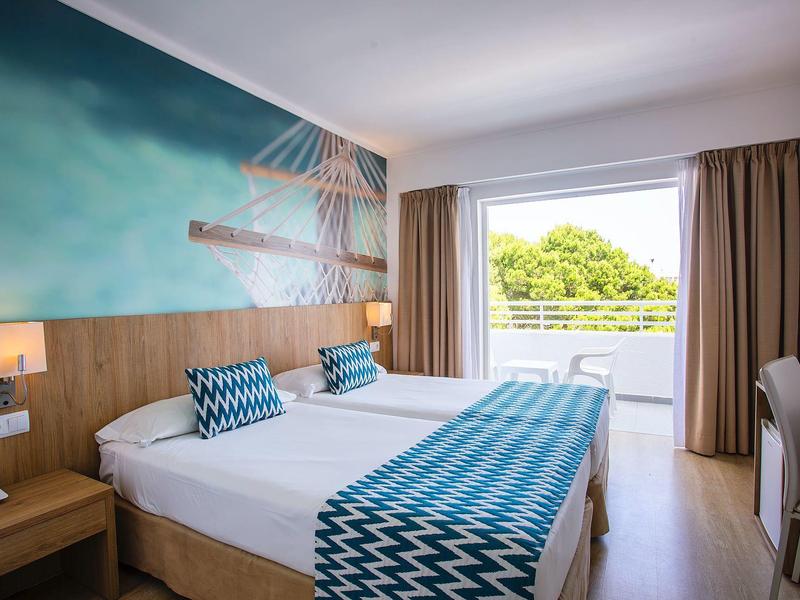 Modernes Hotelzimmer mit Doppelbett, blau-weißem Bettwäsche-Muster und Balkon mit Grünblick.