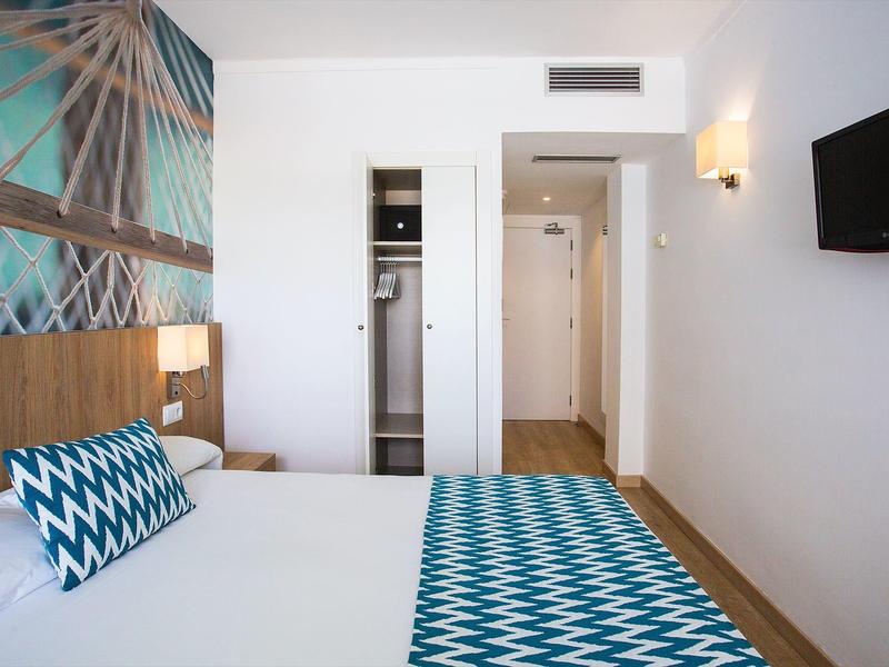 Helles Hotelzimmer mit Doppelbett, türkis-weißem Muster, Wandbild und Wandfernseher.