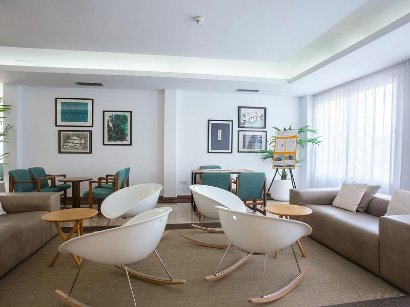 Heller Wohnraum mit großen Fenstern, grauen Sofas, weißen Schaukelstühlen und Holztischen.