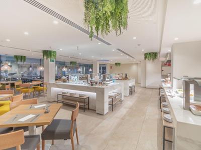 Nowocześnie zaprojektowana restauracja hotelowa z stołami, krzesłami i wiszącymi roślinami.