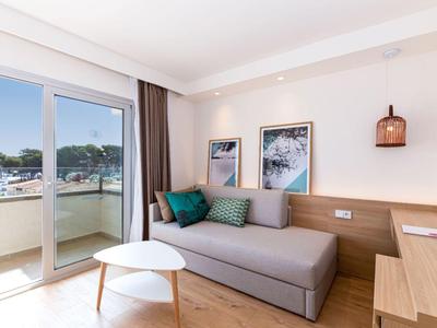 Jasny salon z szarą kanapą, białymi stolikami, sztuką na ścianie i dostępem do balkonu z widokiem na morze.