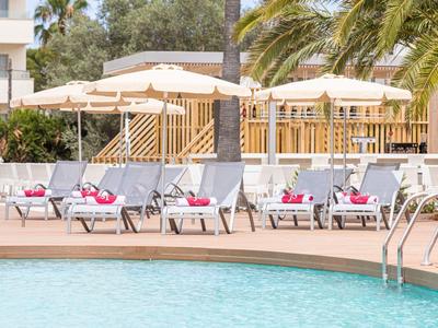 Kilka leżaków z różowymi ręcznikami obok basenu i parasoli.