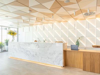 Jasne lobby z nowoczesnym marmurowym i drewnianym biurkiem oraz roślinami.