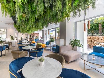 Nowoczesna restauracja hotelowa z niebieskimi siedzeniami i zielonymi wiszącymi roślinami na suficie.