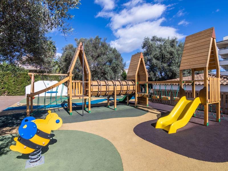 Kolorowy plac zabaw dla dzieci z huśtawkami, zjeżdżalniami i sprężyną w kształcie pszczoły pod niebieskim niebem.