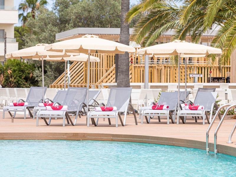 Strefa basenowa z leżakami i parasolami obok hotelu.