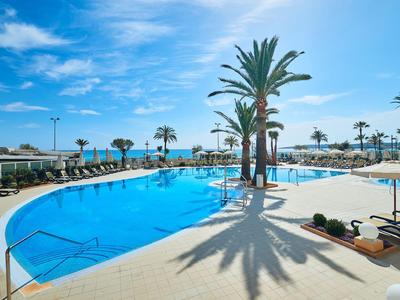 Großer Outdoor-Pool mit Palmen und Sonnenliegen unter klarem blauem Himmel in einem Hotelurlaub.