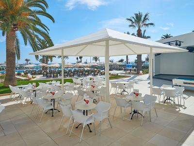 Außenbereich einer Hotelterrasse mit weißen Tischen und Stühlen unter einem großen Sonnenschirm.