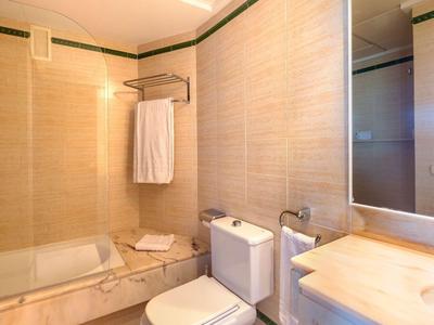Kompaktes Badezimmer mit Badewanne, Toilette und Waschtisch, beige Fliesen und Handtüchern.