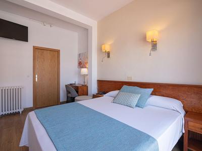 Camera d'hotel moderna con letto matrimoniale, due lampade da parete e TV a muro.