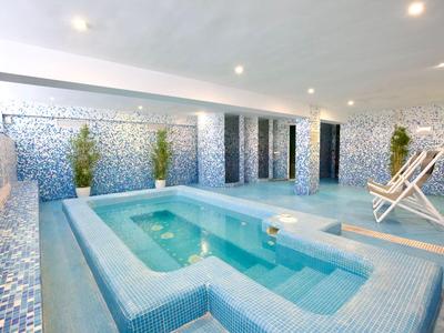 Piscina interna moderna con pareti piastrellate blu e sedie a sdraio in hotel
