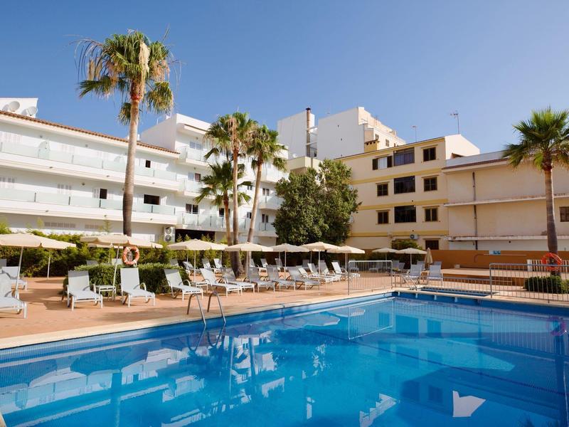 Piscina del hotel con sombrillas, tumbonas y palmeras bajo cielo despejado.