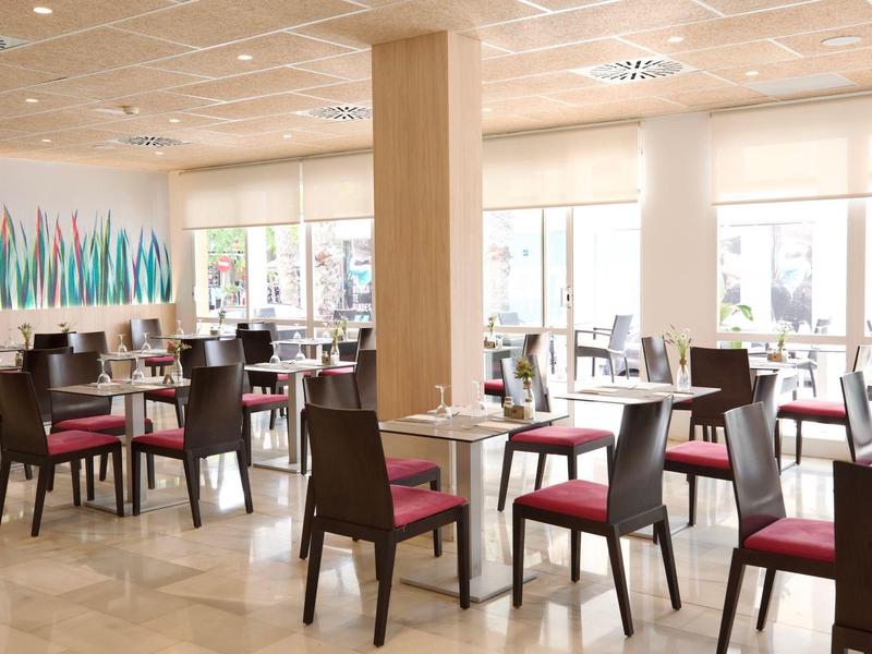 Restaurante moderno y luminoso con muebles de madera y cojines rojos, mucha luz natural.