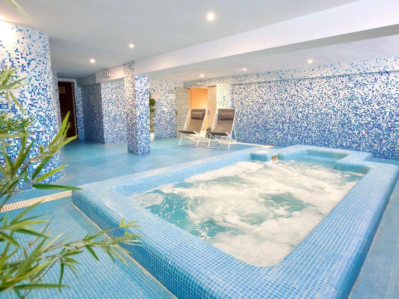Interior de un área de spa con jacuzzi y mosaicos azules en el suelo y las paredes.