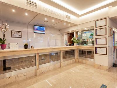 Heller Empfangsbereich mit langer Holztheke, Fernseher an der Wand und Pflanzen als Dekoration.