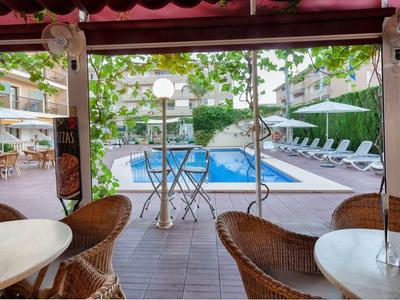 Uitzicht vanaf een overdekt terras op een zwembad met ligstoelen en groene omgeving.