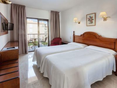 Jasny pokój hotelowy z dwoma pojedynczymi łóżkami, balkonem i prostym drewnianym wystrojem.