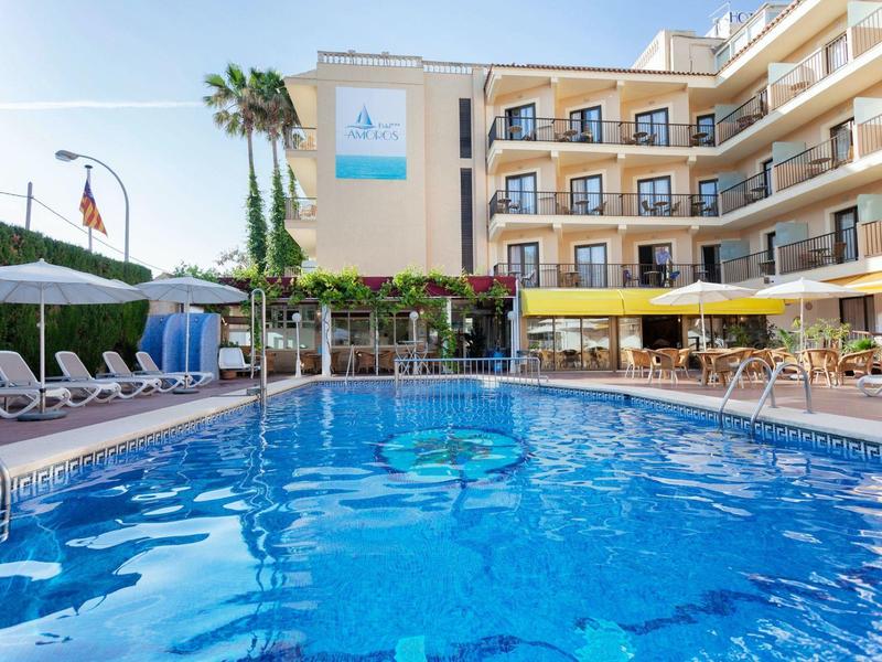 Hotel z basenem na świeżym powietrzu, leżakami i parasolami pod palmami przy bezchmurnym niebie.