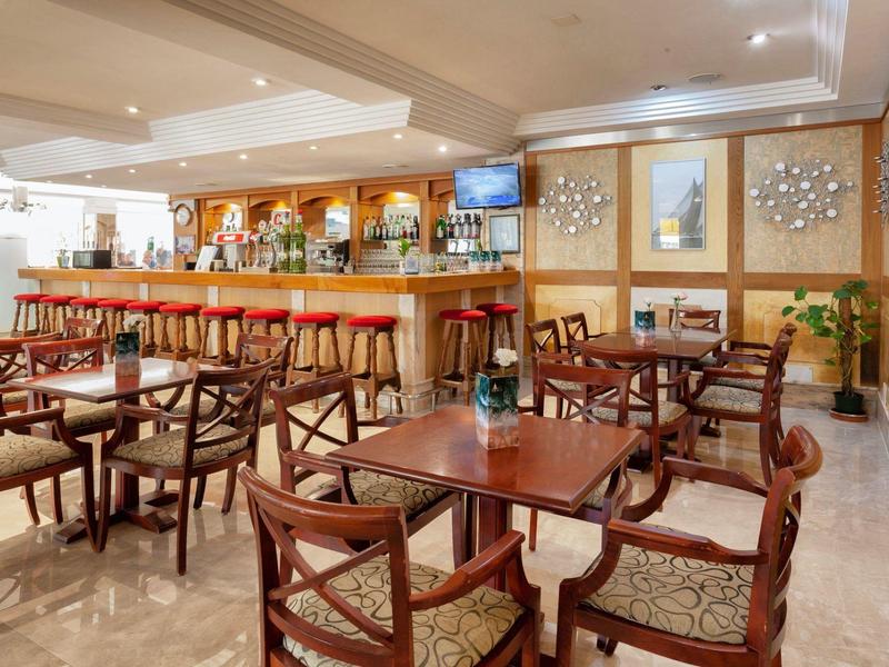 Elegancki bar hotelowy z drewnianymi stołami i wygodnymi krzesłami w ciepłym oświetleniu.