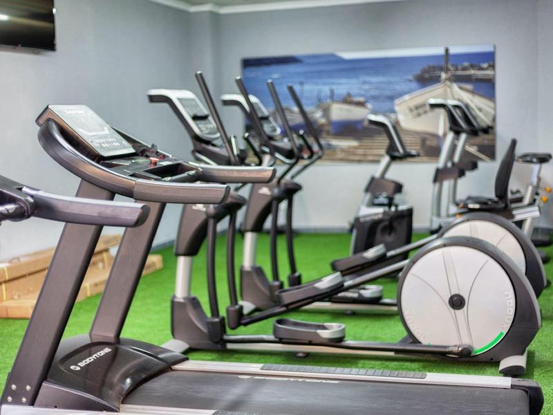 Siłownia z bieżniami i rowerami przed muralem morza