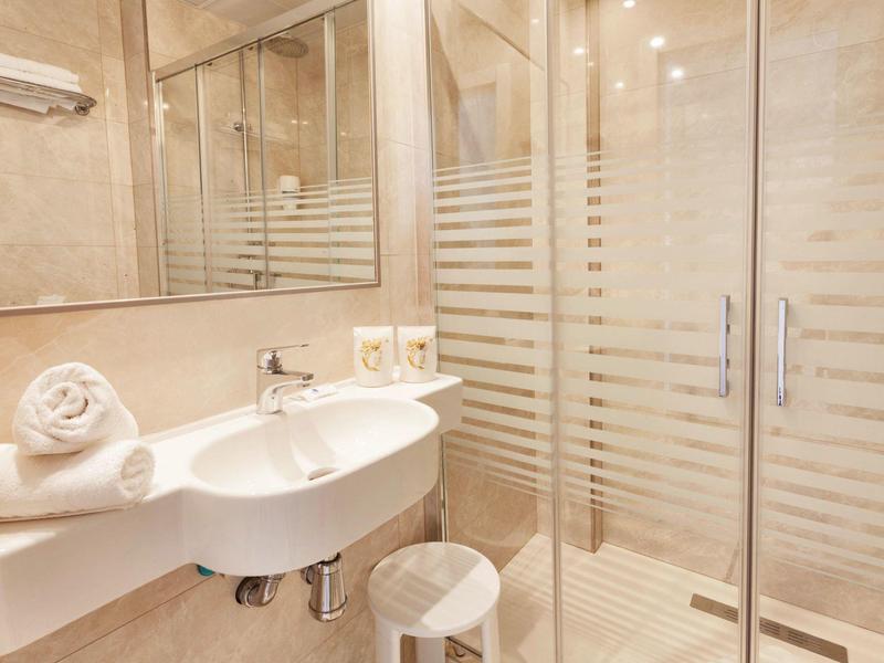 Jasna łazienka z umywalką, lustrem, ręcznikami i prysznicem z przeszklonymi drzwiami.