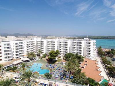 Große weiße Hotelanlage mit Pool, Palmen und Blick auf das blaue Meer unter blauem Himmel.