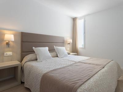 Moderní hotelový pokoj s manželskou postelí, neutrálními tóny a přirozeným světlem z okna.