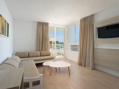 Jasný obývací pokoj se dvěma pohovkami, konferenčním stolkem, televizí a balkonem s výhledem na moře.