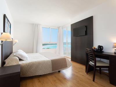 Moderní hotelový pokoj se dvěma lůžky, psacím stolem, televizí a výhledem na moře skrz velká okna.