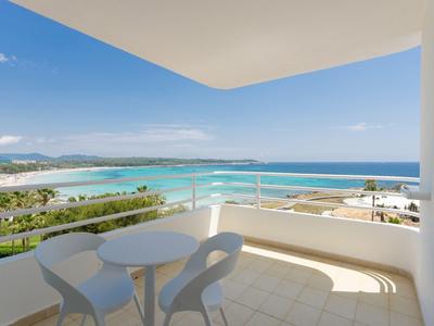 Balkon s malým stolem a židlemi s výhledem na moře pod modrou oblohou.