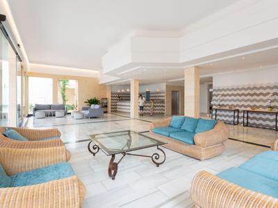 Helle Hotellobby mit Korbsesseln, blauen Sofas und einem Glastisch.