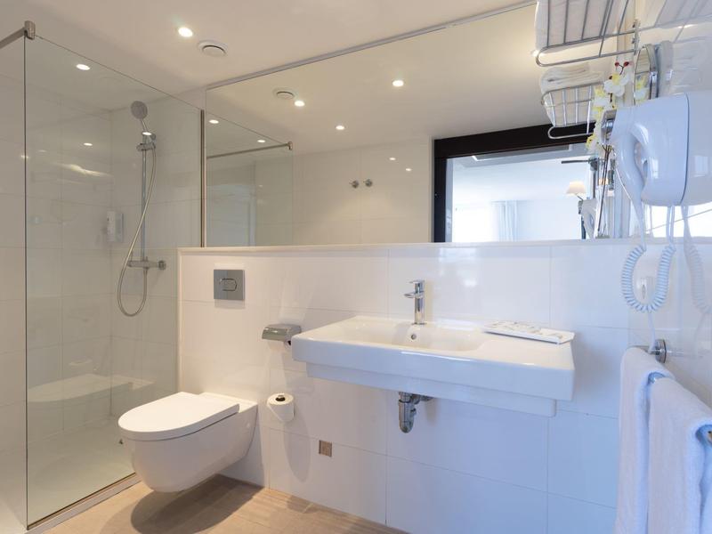 Moderní koupelna se sprchovým koutem ze skla, závěsnou toaletou a bílým umyvadlem.