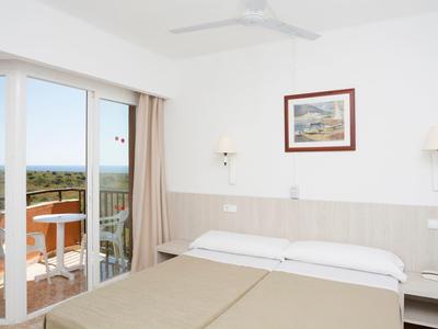 Camera d'hotel luminosa con balcone vista mare e letti singoli.