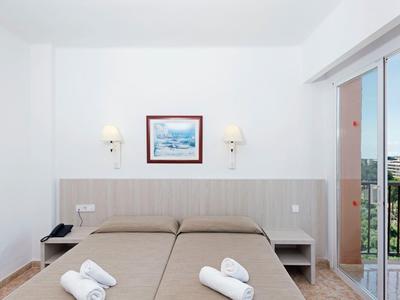 Camera d'hotel con letti singoli, asciugamani piegati e vista sul balcone soleggiato.