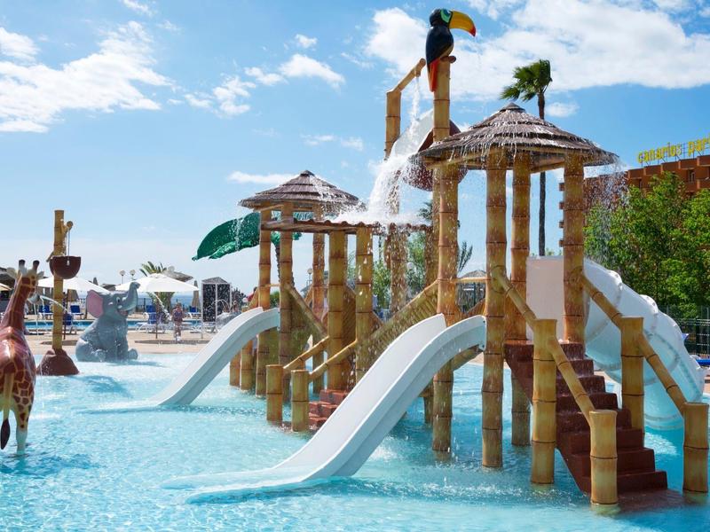Area giochi acquatica con scivoli, fontane e animali di legno in piscina.