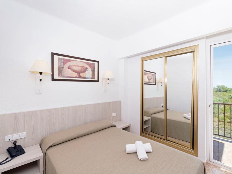 Camera d'hotel semplice con letto matrimoniale, quadro, specchio e balcone con vista sulla natura.