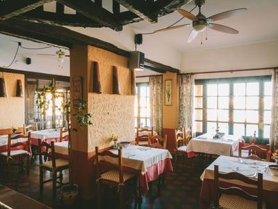 Gemütliches Restaurant mit Holzbalken, weißen Tischdecken und großen Fenstern.