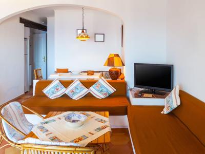 Heller Wohnraum mit brauner Polsterecke, Holzlampe, kleinem Fernseher und geflochtenem Sessel mit Tisch.