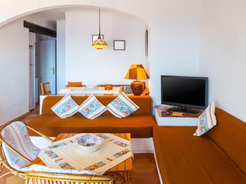 Heller Wohnraum mit brauner Polsterecke, Holzlampe, kleinem Fernseher und geflochtenem Sessel mit Tisch.