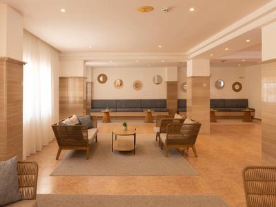 Jasna przestrzeń lobby hotelowego z fotelami, sofami i dekoracyjnymi lustrami na ścianach.