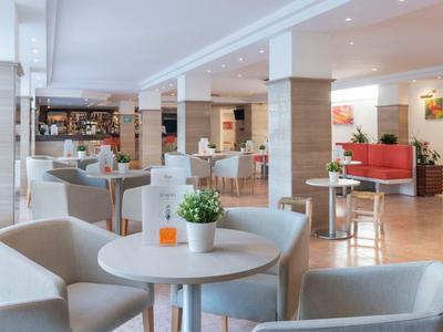 Nowoczesny salon hotelowy z białymi fotelami, stołami i dekoracyjnymi roślinami.