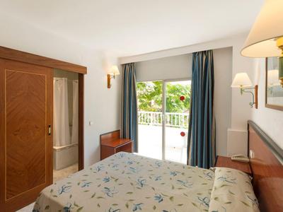 Mały pokój hotelowy z podwójnym łóżkiem, drzwiami przesuwnymi, stolikiem nocnym i widokiem na balkon i ogród.