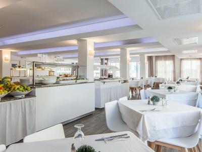 Ein heller, moderner Speisesaal mit rund gedeckten Tischen, weißen Tischdecken und Buffetbereich.