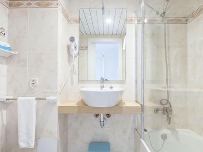 Helles Badezimmer mit weißem Waschbecken, Spiegel, Badewanne und Duschwand aus Glas.